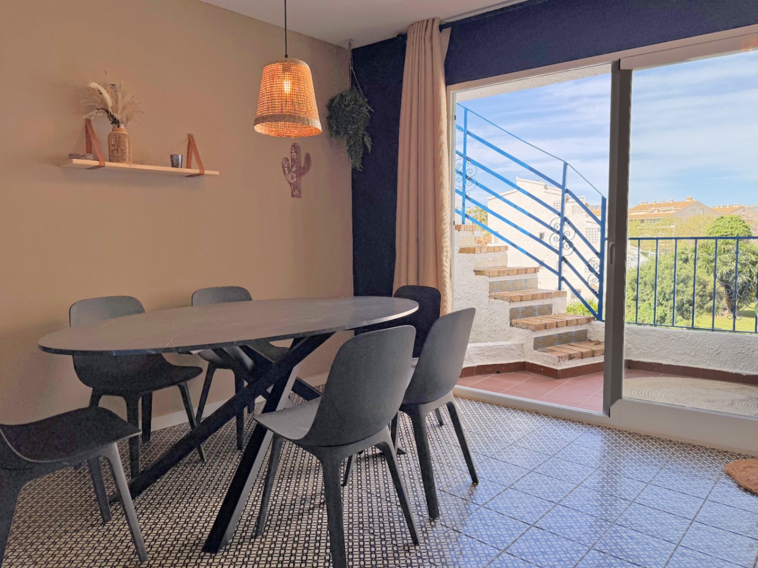 Comedor con mesa ovalada negra y acceso a terraza con escalera exterior y barandilla azul.