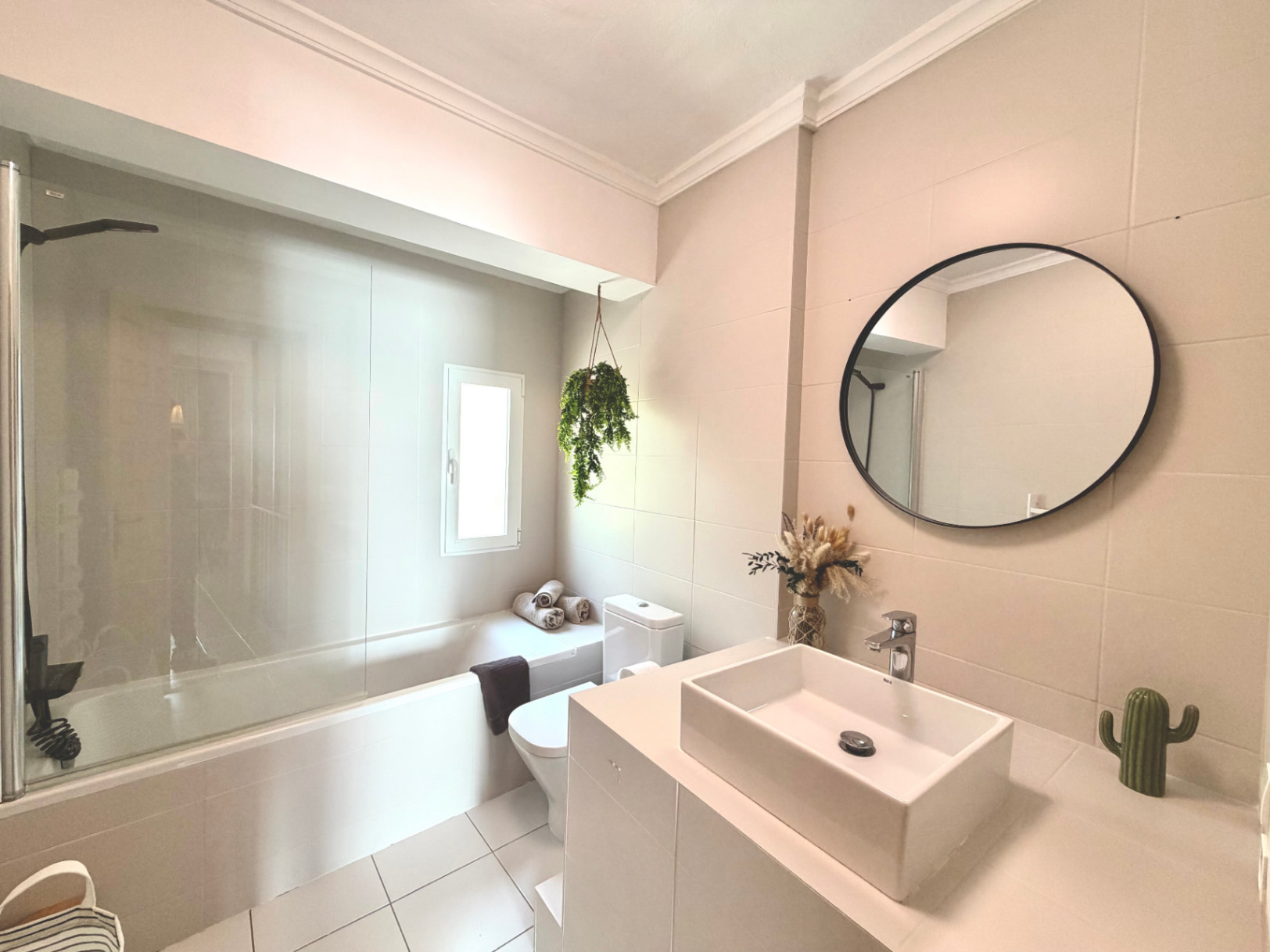 Cuarto de baño luminoso con bañera, lavabo moderno y espejo circular. Decoración minimalista con toques naturales.