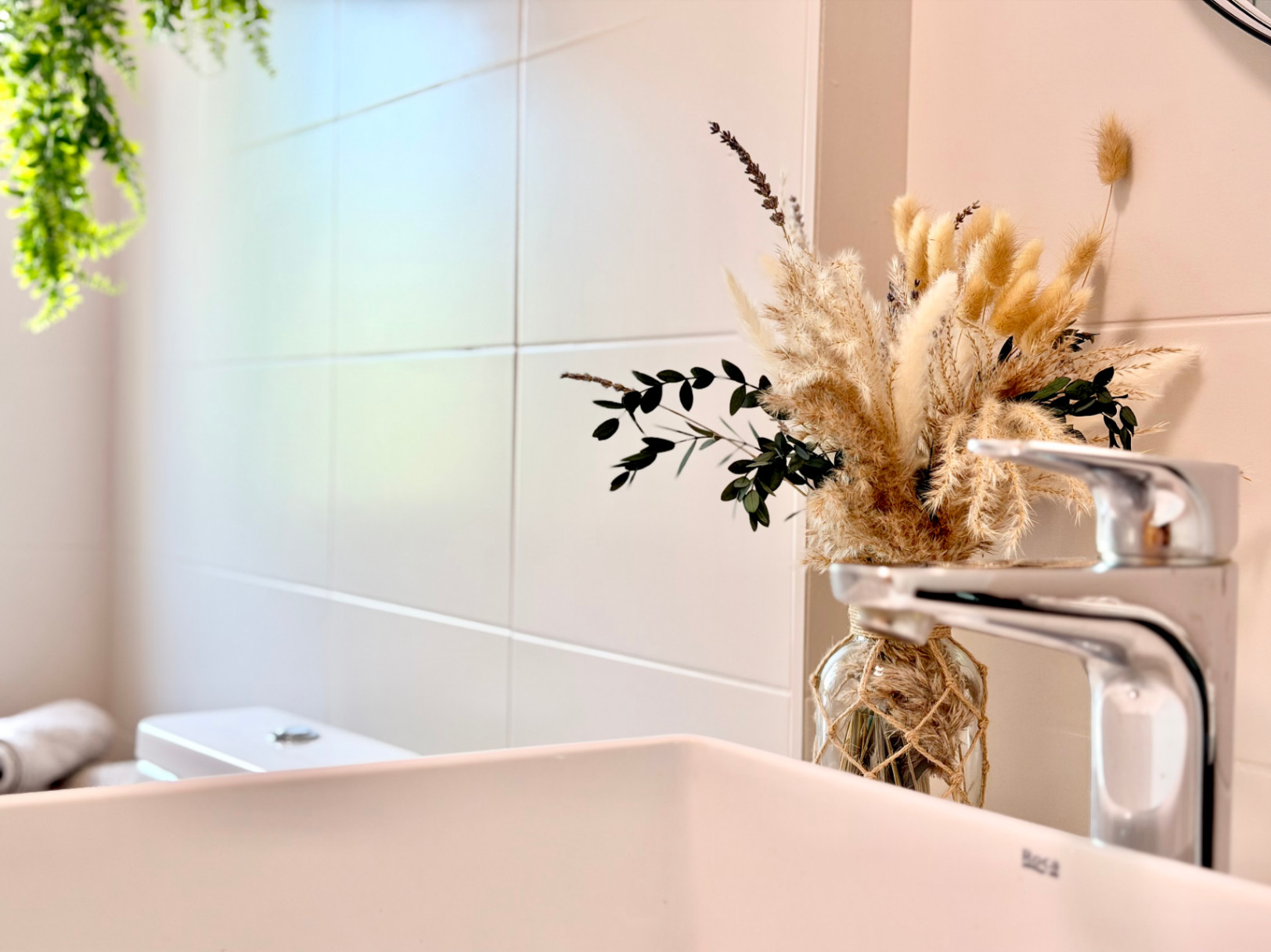 Detalle de baño con lavabo blanco, grifo moderno y decoración floral minimalista.