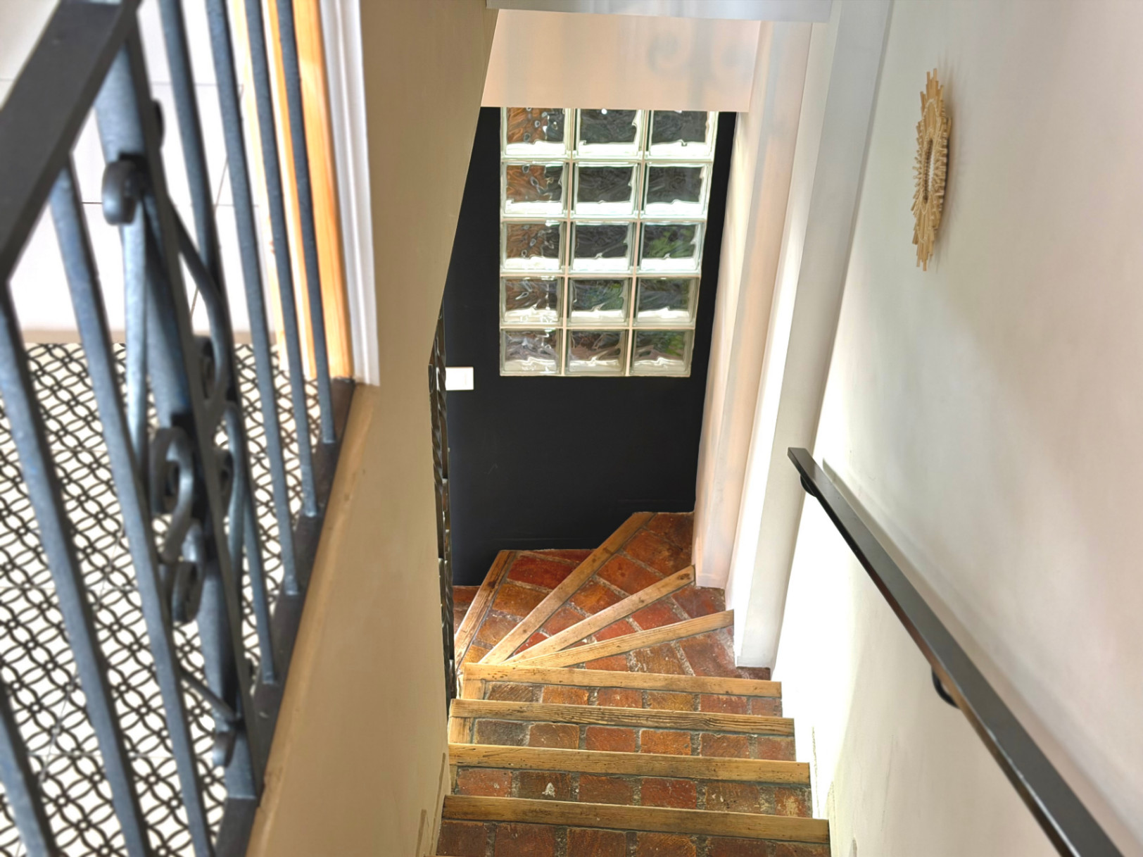 Detalle de escalera interior con peldaños de ladrillo y barandilla de hierro forjado.