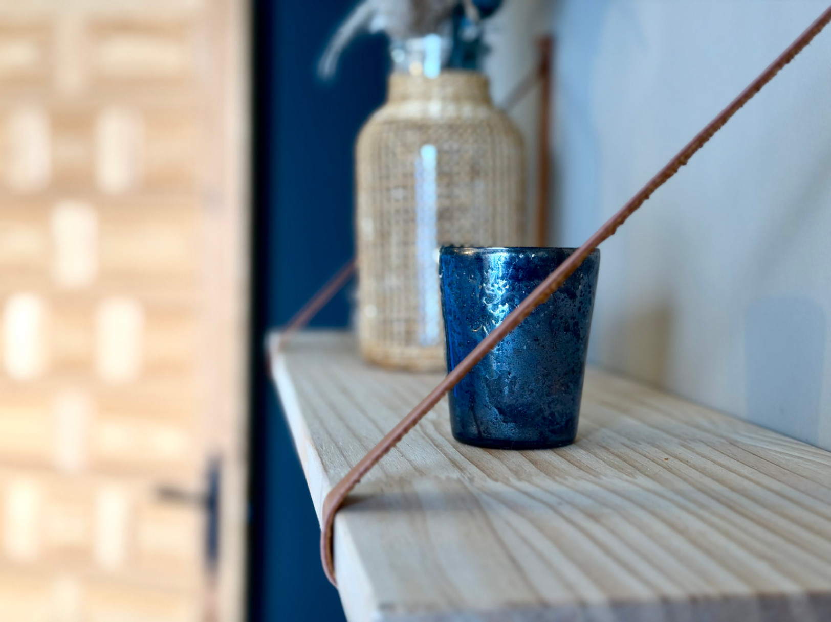 Detalle de estante de madera con vaso decorativo azul y botella de mimbre en segundo plano.