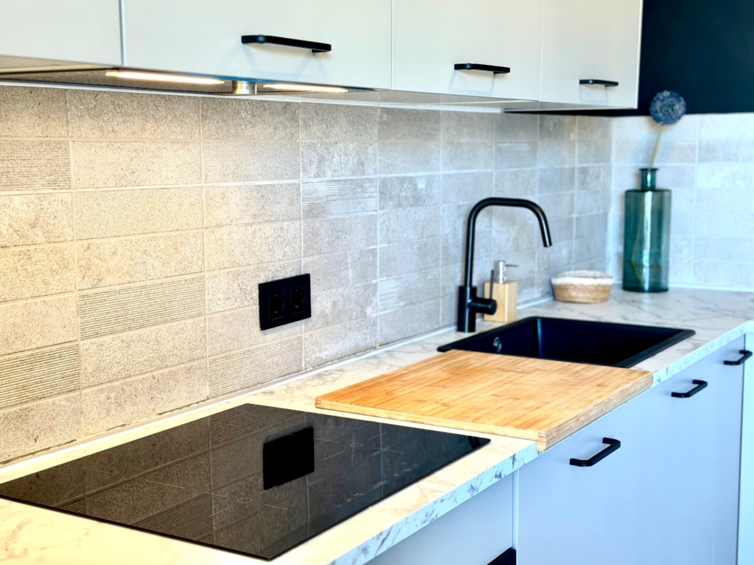 Detalle de la cocina reformada con encimera de mármol, fregadero negro y placa de inducción.