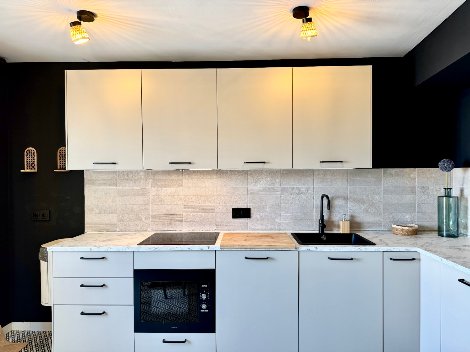 Detalle de la cocina renovada con encimera de mármol, armarios claros y pared negra contrastante.
