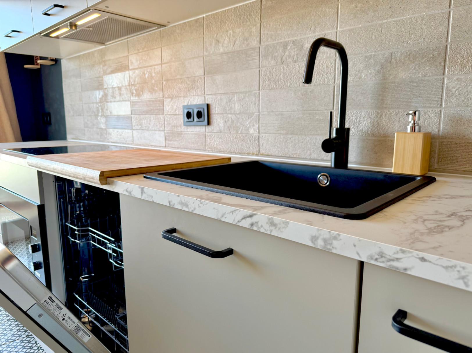 Detalle de la cocina renovada con fregadero negro, encimera de mármol y protector contra salpicaduras de azulejos texturizados.