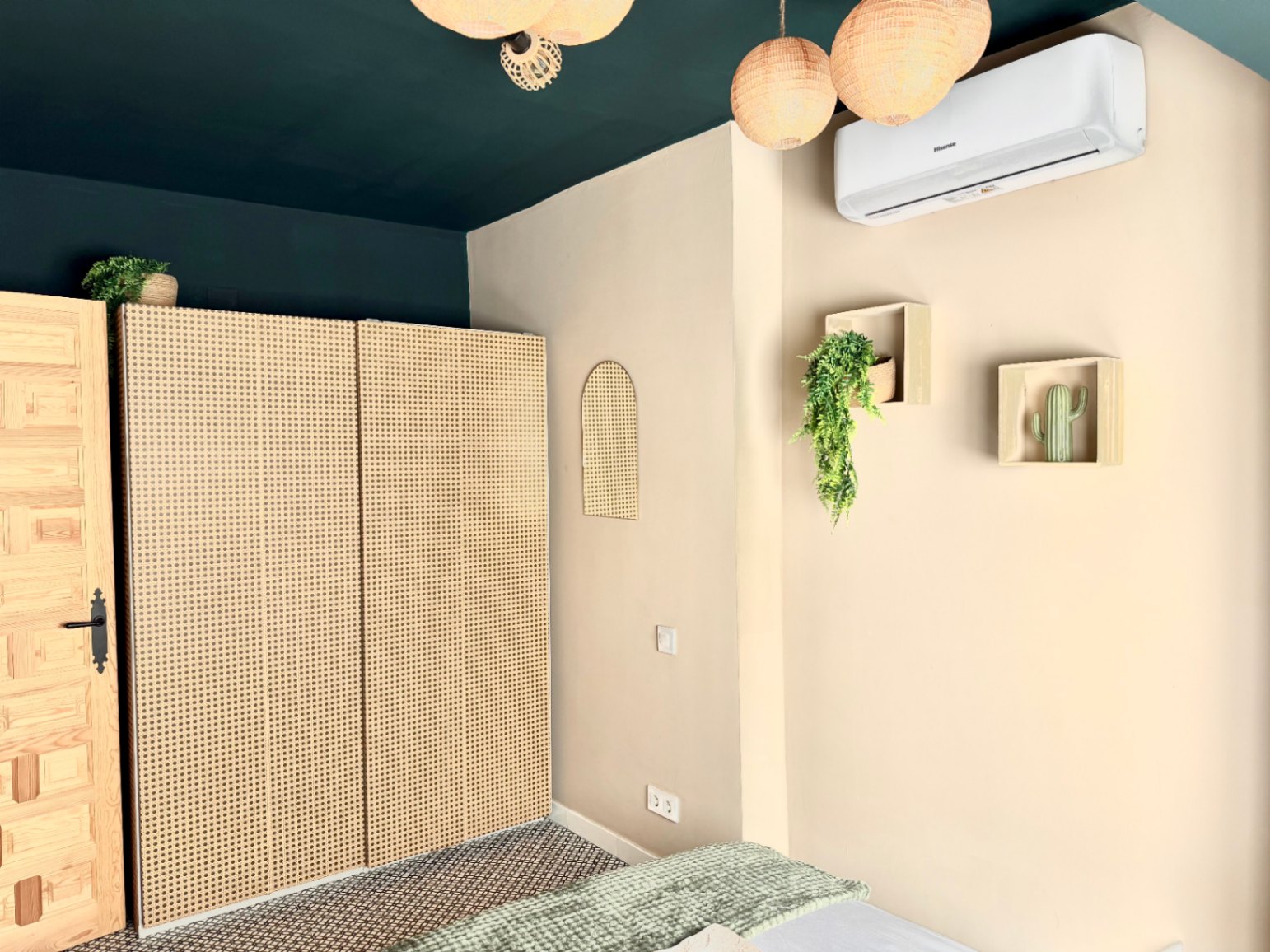 Dormitorio con armario de ratán, techo verde oscuro y decoración mural minimalista.
