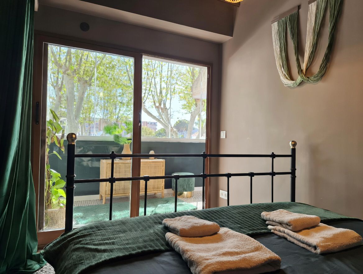 Dormitorio con cama de hierro forjado y terraza con vistas arboladas. Decoración minimalista en tonos neutros y verdes.