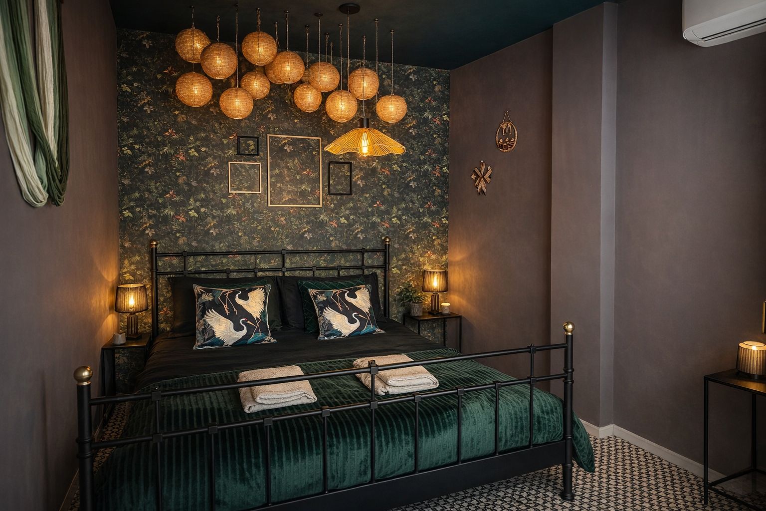 Dormitorio con papel pintado floral, cama de hierro forjado, colcha de terciopelo verde y lámparas de noche.
