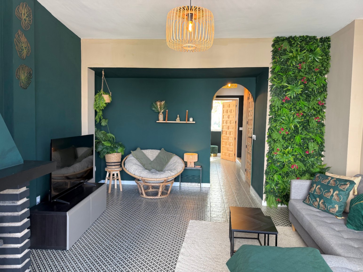 Salón con pared verde vertical, suelo de baldosas estampadas y decoración en tonos verdes y madera.