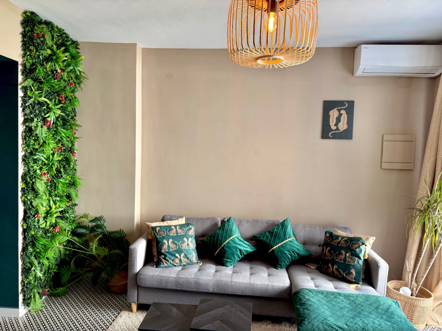 Salón moderno con pared verde vertical, sofá gris con cojines verdes y lámpara de techo de madera.