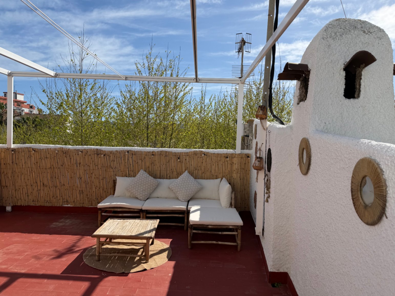 Terraza con suelo rojo, asientos de bambú y pared blanca decorada con círculos de esparto.