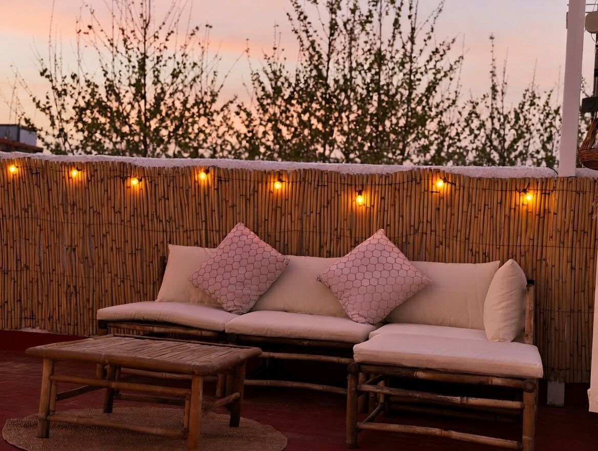 Terraza privada con cerramiento de bambú y luces cálidas, amueblada con sofá y mesa de centro de bambú.