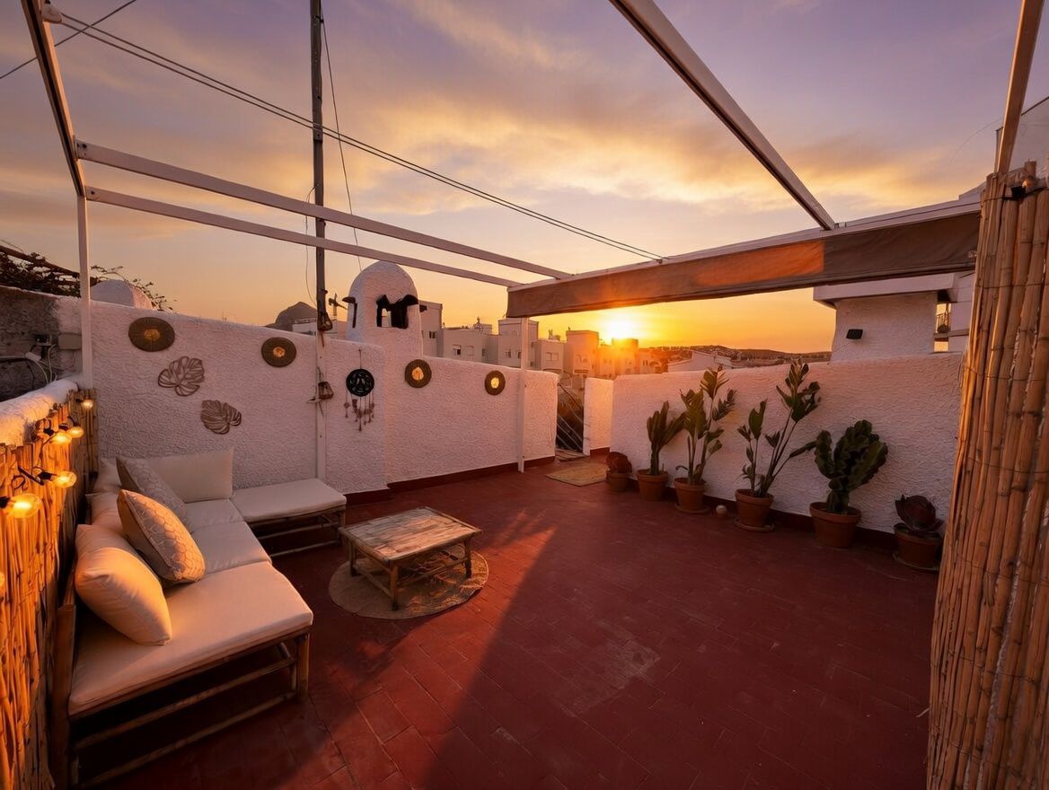 Terraza privada con suelo de terracota, decorada con plantas en macetas y mobiliario de bambú, con vistas al atardecer.