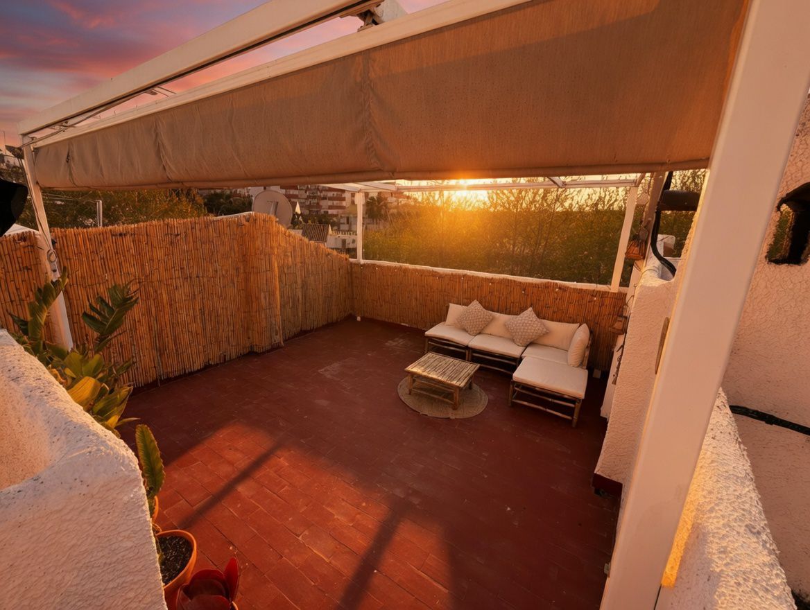 Terraza privada con toldo, suelo de baldosas rojas y valla de bambú. Incluye sofá modular y mesa de centro.