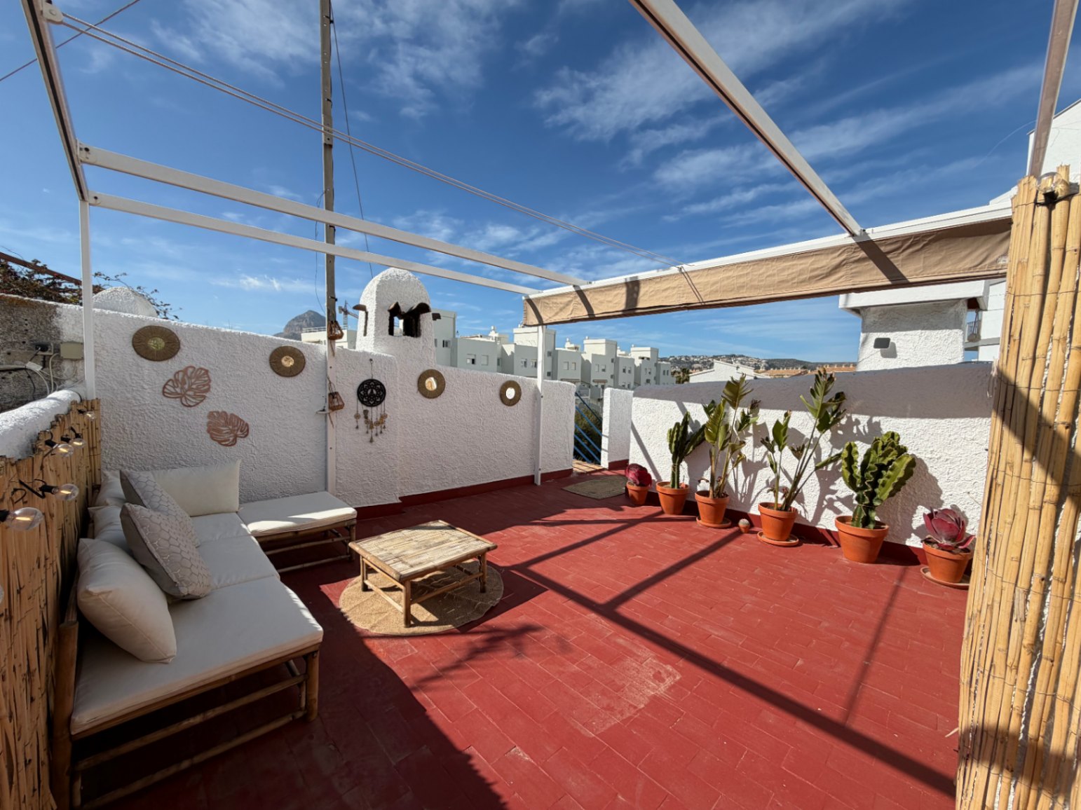 Terraza soleada con suelo de terracota, sofá de bambú y plantas en macetas, ideal para disfrutar del aire libre.
