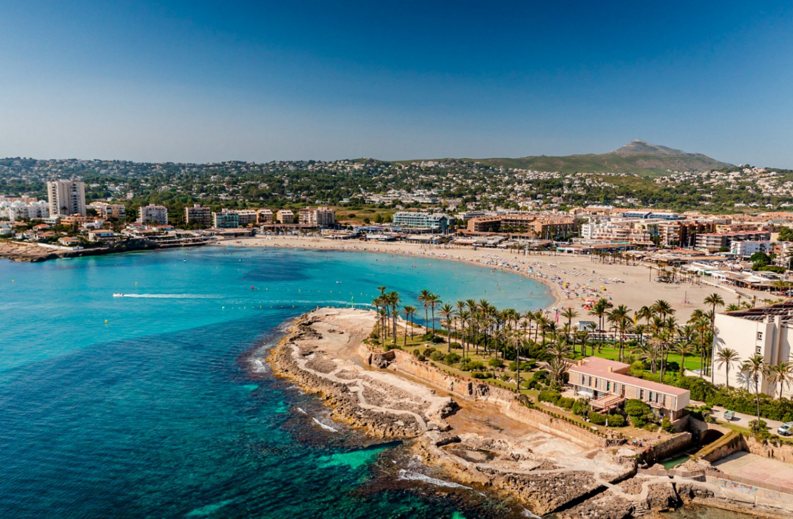 Vista aérea de la Playa del Arenal en Jávea, con aguas turquesas y edificios costeros.
