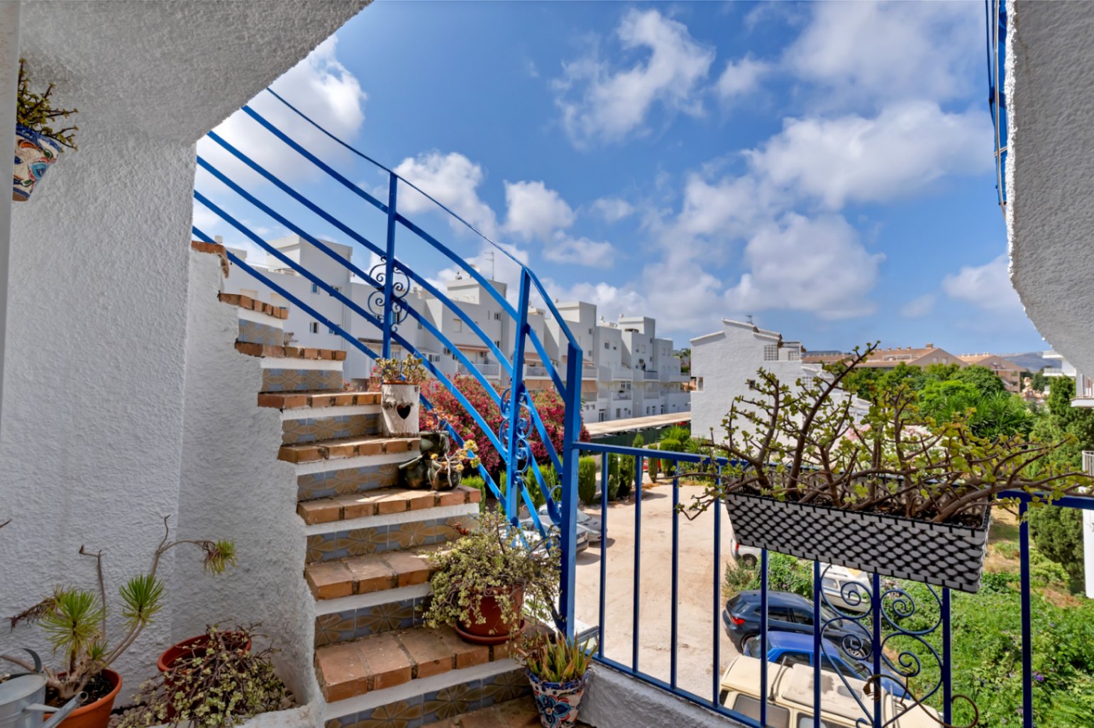 Vista de la escalera exterior con barandilla azul, detalles de cerámica y plantas ornamentales.