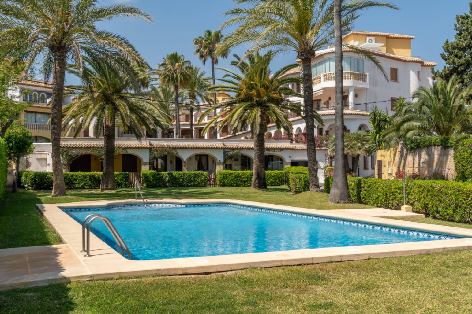 Piscina comunitaria con césped y palmeras en urbanización de Jávea.
