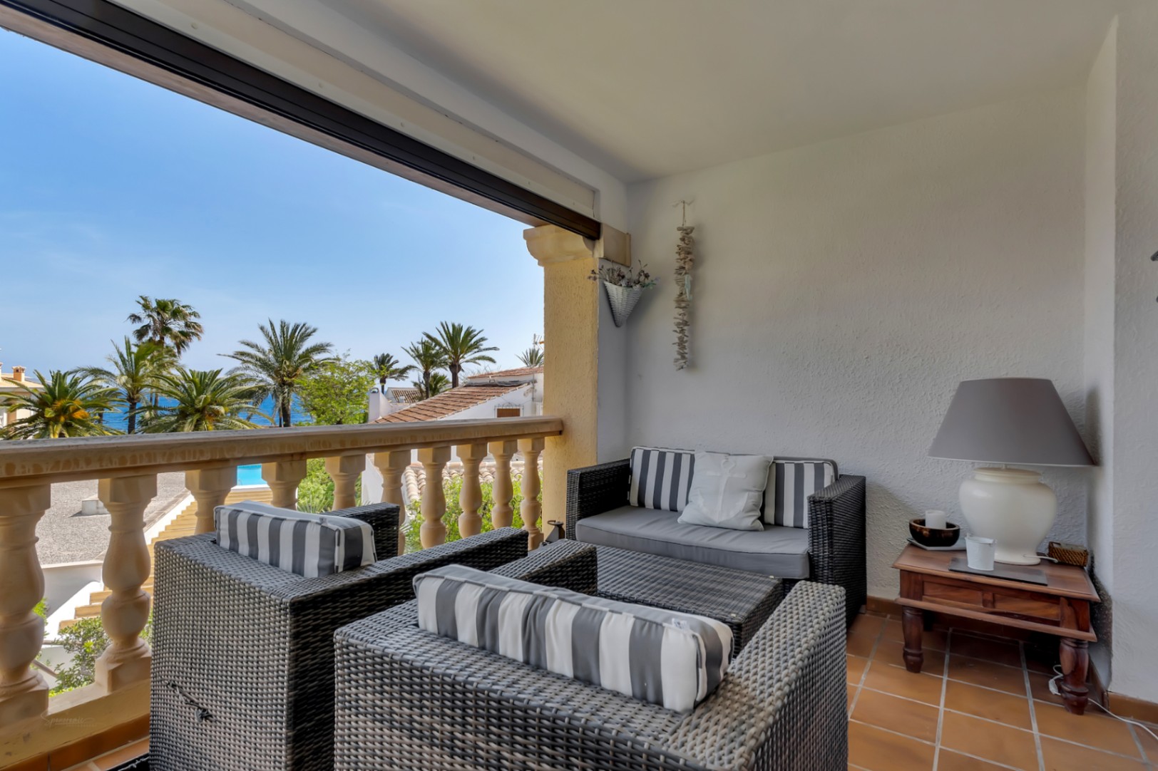 Terraza con vistas al mar, amueblada con sillones de mimbre y cojines a rayas, ideal para relajarse.
