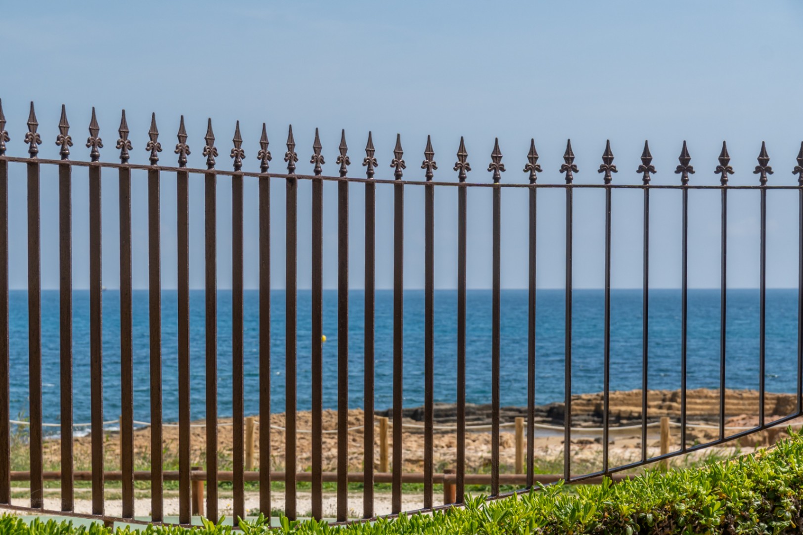 Vista al mar Mediterráneo a través de una valla de hierro forjado con detalles ornamentales.