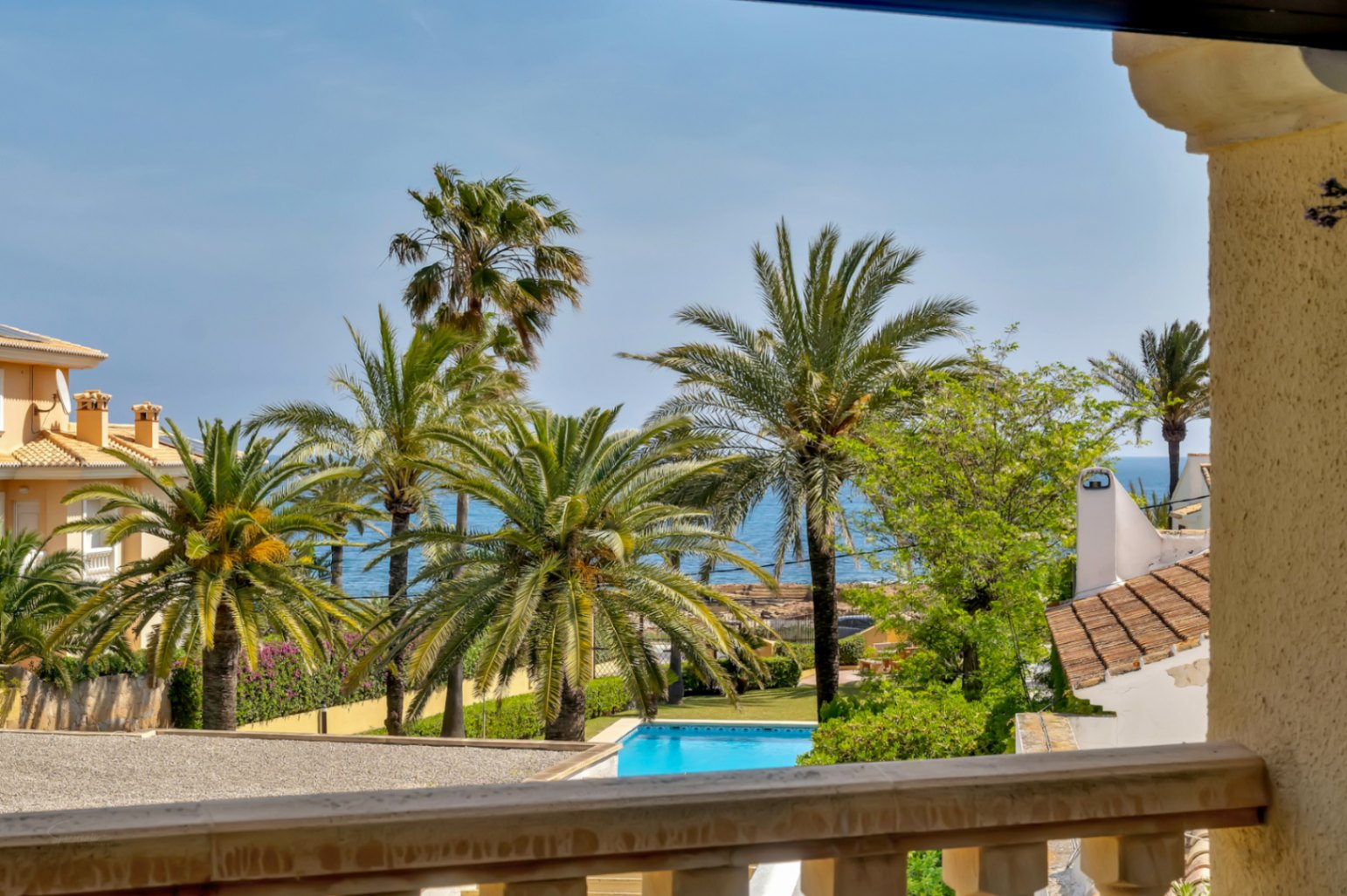 Vistas desde la terraza a la piscina comunitaria y palmeras, con el Mediterráneo al fondo.