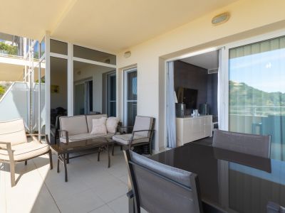 Amplia terraza exterior con dos zonas diferenciadas: un lounge con sofá y sillones, y un comedor con mesa oscura. Ofrece vistas a la vegetación y acceso directo al interior.
