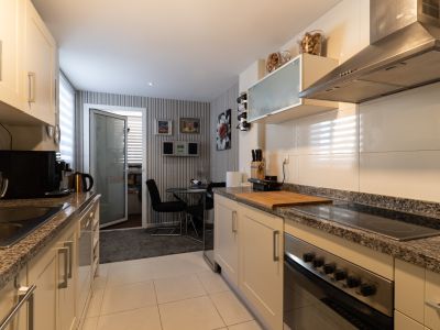 Cocina equipada con muebles crema, encimeras de granito y electrodomésticos de acero inoxidable. Al fondo, zona de comedor con mesa de cristal y papel pintado a rayas.