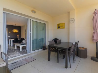 Terraza exterior con suelo de baldosas claras, mesa de comedor oscura y parasol plegado, conectada a un salón interior con lámpara colgante dorada.