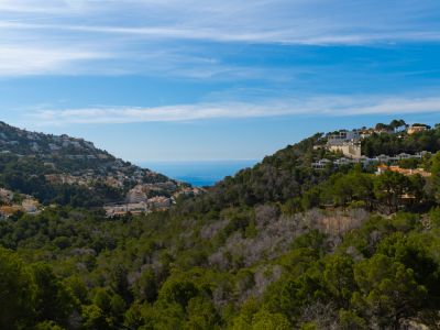 Vista panorámica de Altea Hills, mostrando edificios residenciales entre laderas verdes y el mar Mediterráneo en el horizonte bajo un cielo despejado.