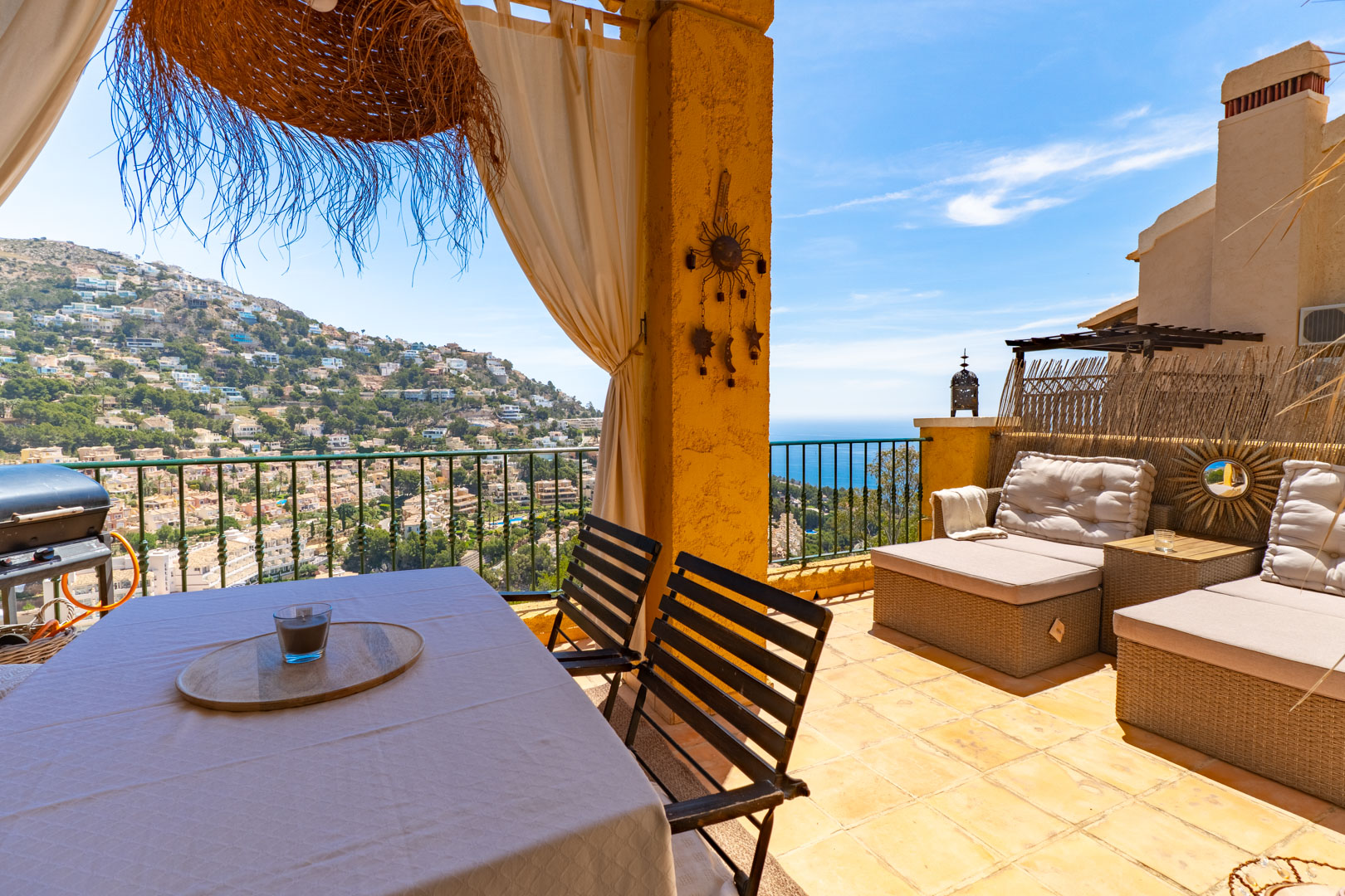 Amplia terraza exterior con mesa de comedor, barbacoa y zona lounge, ofreciendo vistas panorámicas a la colina residencial y al mar Mediterráneo.