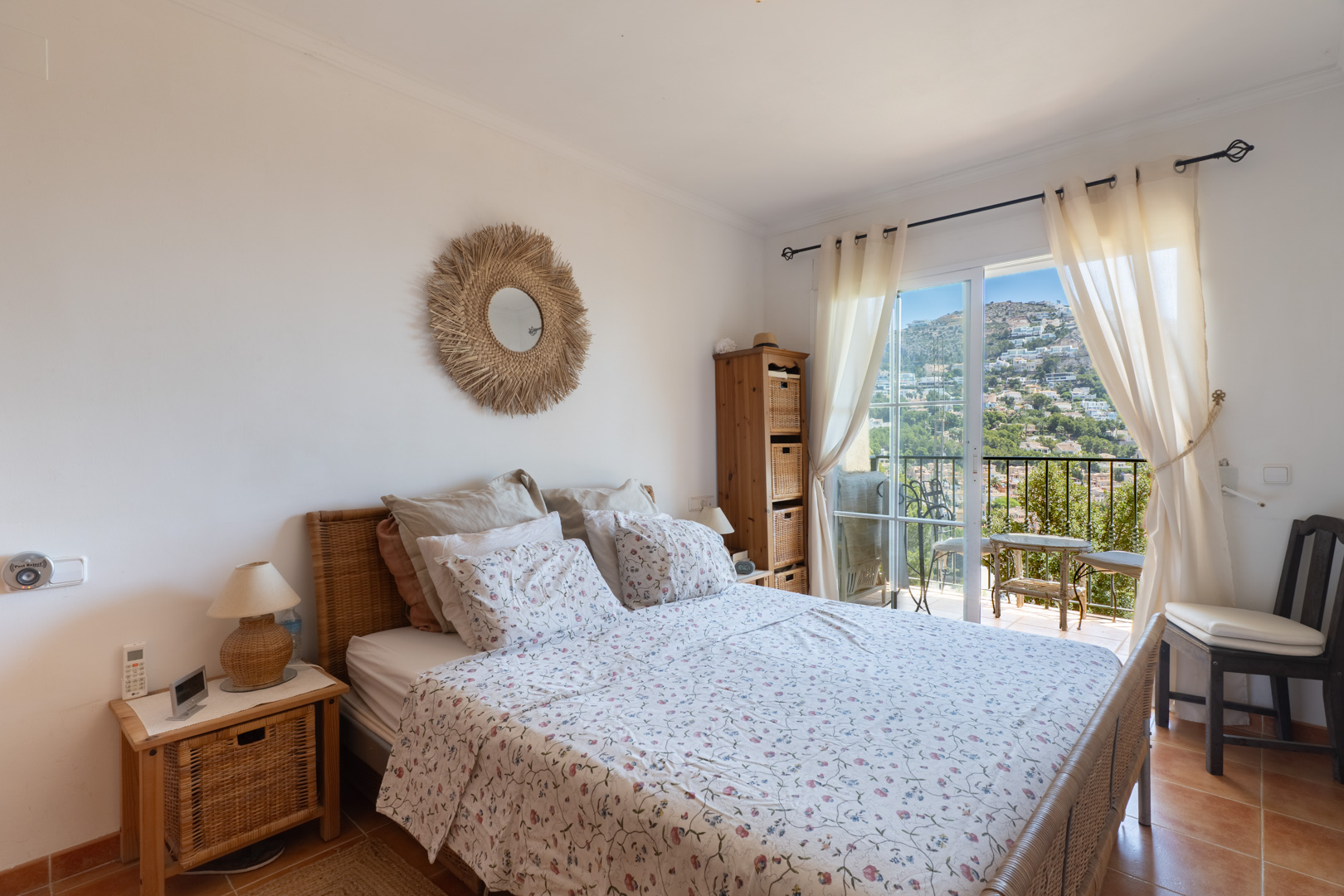 Luminoso dormitorio con cama y cabecero de mimbre, acceso directo a balcón privado. Ofrece suelos de gres y vistas panorámicas a la colina de Altea Hills.