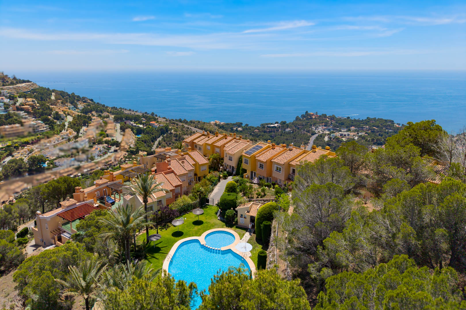 Vista aérea del complejo residencial en Altea Hills, con una piscina comunitaria de forma distintiva, exuberantes jardines y vistas panorámicas al mar Mediterráneo.