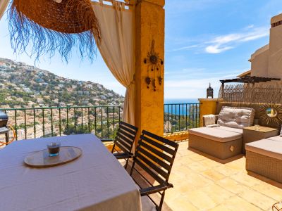 Amplia terraza exterior con mesa de comedor, barbacoa y zona lounge, ofreciendo vistas panorámicas a la colina residencial y al mar Mediterráneo.