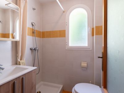 Baño compacto con ventana arqueada de cristal esmerilado, paredes alicatadas en dos tonos con franja naranja, ducha con plato y mueble de lavabo de madera.