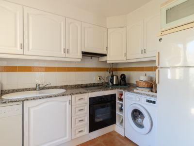 Cocina funcional con armarios blancos de paneles, encimera de granito, electrodomésticos integrados y azulejos con franja decorativa naranja.