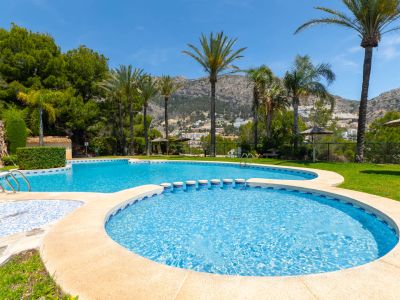 Complejo de piscinas de varios niveles con área infantil, rodeado de palmeras y césped. Ofrece vistas panorámicas a las montañas y la vegetación local bajo un cielo azul despejado.