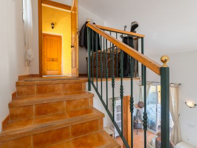 Escalera interior con peldaños de azulejo terracota y borde de madera, destacando una barandilla de metal verde oscuro y pasamanos de madera. Conduce a una entrada con pared amarilla y puerta de madera.