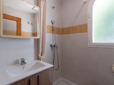 Este baño funcional presenta un mueble de lavabo de madera clara, ducha con cortina y una ventana arqueada de cristal esmerilado, complementado con azulejos blancos y una banda decorativa ocre.