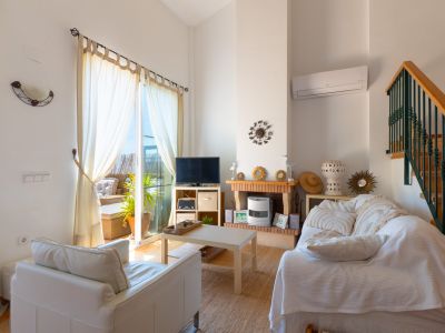 Sala de estar luminosa con techos altos, acceso a terraza, chimenea de ladrillo decorativa y escalera de madera con barandilla verde.