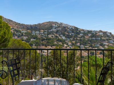 Terraza con barandilla de hierro forjado y mobiliario exterior, ofreciendo vistas panorámicas a la urbanización en la ladera de la montaña.
