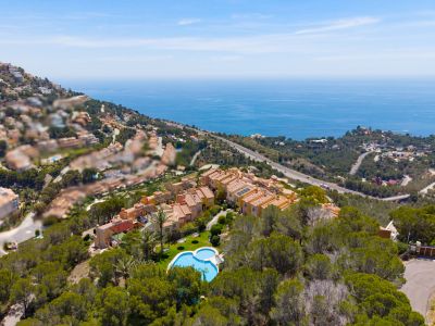 Vista aérea de complejo residencial en ladera con piscina en forma de corazón, rodeado de árboles y vistas panorámicas al mar Mediterráneo.