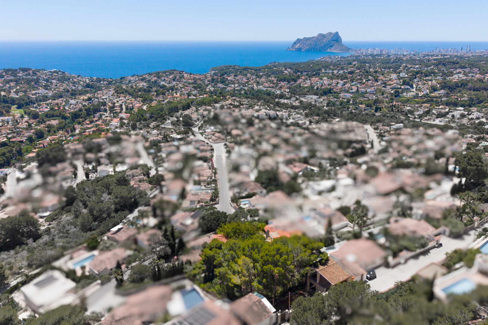 Vista aérea de una zona residencial costera con el mar Mediterráneo y el Peñón de Ifach en la distancia, bajo un cielo azul claro. Vista aérea de una zona residencial costera con el mar Mediterráneo y el Peñón de Ifach en la distancia, bajo un cielo azul claro.