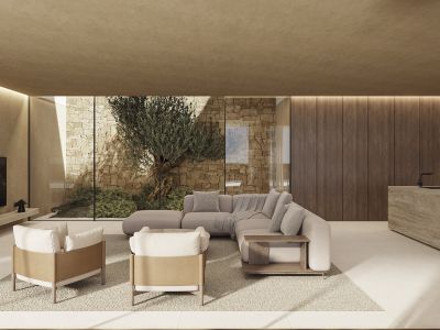Espacioso salón con ventanales que dan a un patio con muro de piedra y olivo. Incluye sofá modular, sillones modernos y una isla de piedra con grifo, complementado por iluminación lineal.