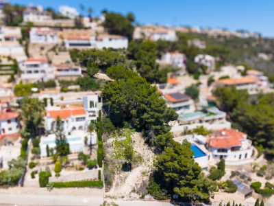 Vista aérea de la urbanización Montemar en Benissa, mostrando villas blancas con tejados de terracota y piscinas, integradas en la ladera verde.