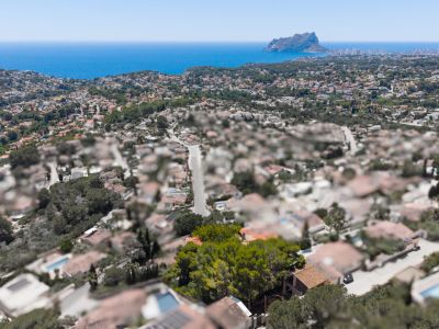 Vista aérea de una zona residencial costera con el mar Mediterráneo y el Peñón de Ifach en la distancia, bajo un cielo azul claro.