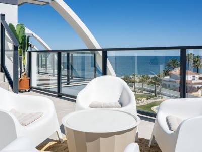 Amplia terraza con mobiliario blanco moderno y barandilla de cristal, ofreciendo vistas panorámicas al mar Mediterráneo y la costa, bajo un distintivo arco estructural.