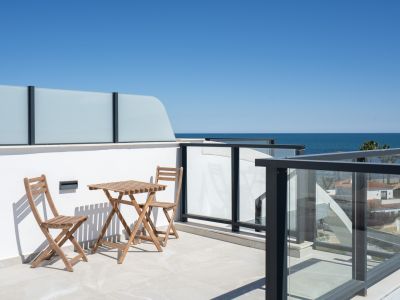 Amplia terraza con suelo de baldosas claras, mobiliario exterior de madera y modernas barandillas de cristal con vista panorámica al mar Mediterráneo.