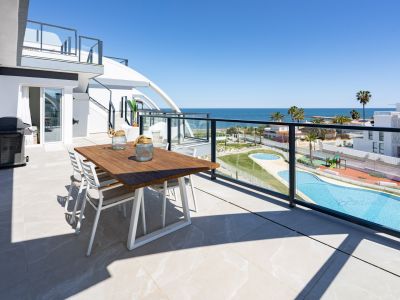 Amplia terraza exterior con mesa de comedor de madera y barbacoa, ofreciendo vistas panorámicas al mar Mediterráneo y a las piscinas comunitarias.