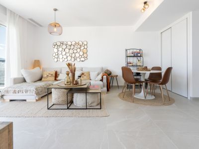 Amplio salón-comedor de planta abierta con sofá seccional claro, un distintivo espejo de círculos y una mesa de comedor redonda con sillas modernas. Grandes ventanales proporcionan luz natural y vistas a la montaña.
