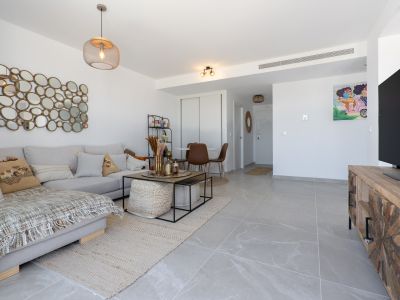 Amplio salón-comedor de planta abierta con suelos de gres porcelánico gris, sofá en L y un distintivo mural de espejos. El espacio integra una mesa de centro moderna y un rincón de comedor compacto.