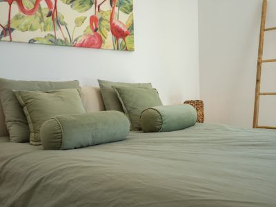 Dormitorio con cama vestida en tonos verde salvia, complementado por un cuadro de flamencos rosas y una escalera decorativa de bambú.
